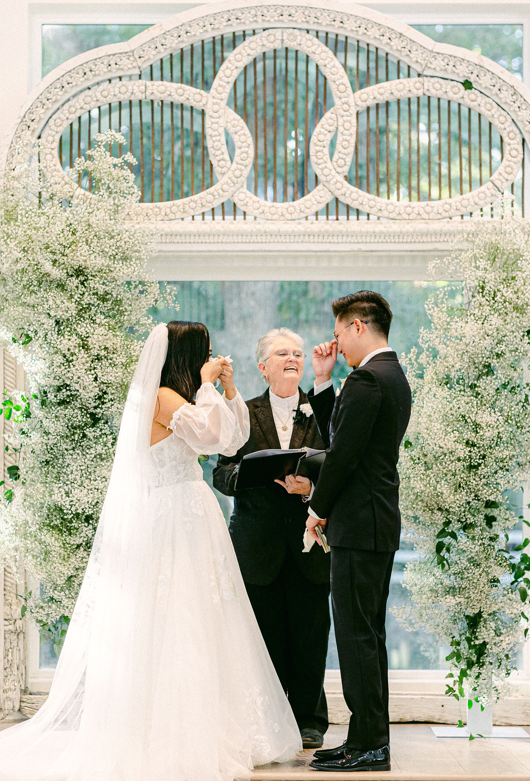 bride and groom tearing up while officiant smiles